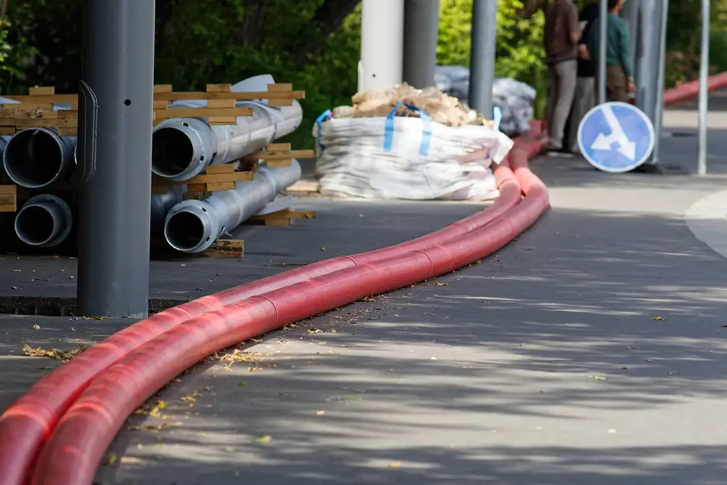 Eletrodutos corrugados vermelhos assentados ao longo de uma calçada, com tubos empilhados ao fundo.