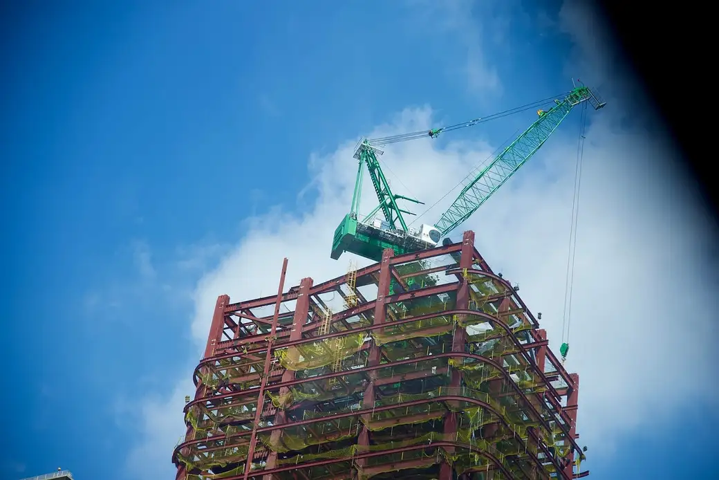 Edifício em estrutura metálica em construção, com guindaste de torre ao lado.